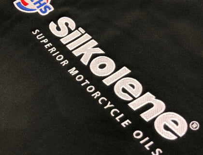 Close-up of embroidered Silkolene Superior Motorcycle Oils branding on a black Fuchs Lubricants work jacket