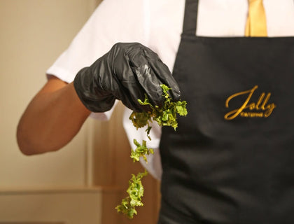 Chef in a black Jolly Catering apron with gold embroidered logo plating food at an event