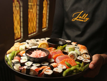 Event server wearing a black embroidered Jolly Catering apron and carrying a sushi and seafood platter