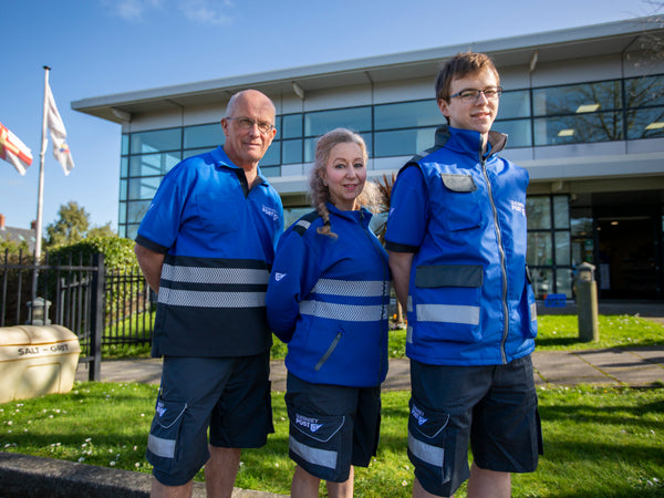 Three Guernsey Post staff outside their headquarters wearing the bespoke hi-vis polo, fleece and gilet range with reflective banding and branded cargo shorts