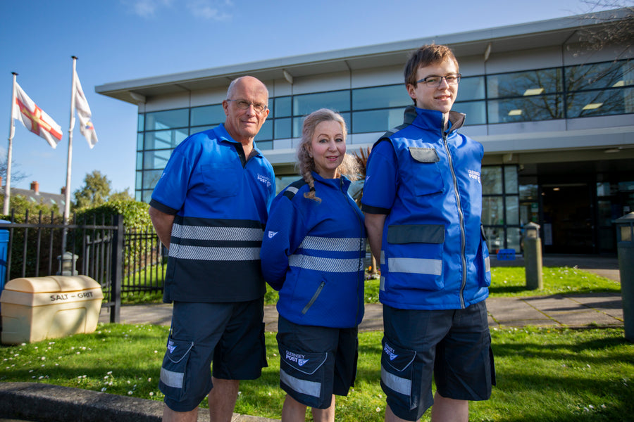 Three Guernsey Post staff outside their headquarters wearing the bespoke hi-vis polo, fleece and gilet range with reflective banding and branded cargo shorts