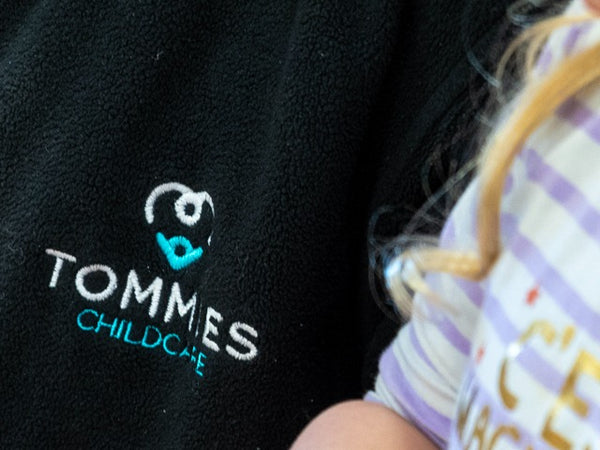 Tommies Childcare logo embroidered on a navy staff fleece, worn in a nursery setting