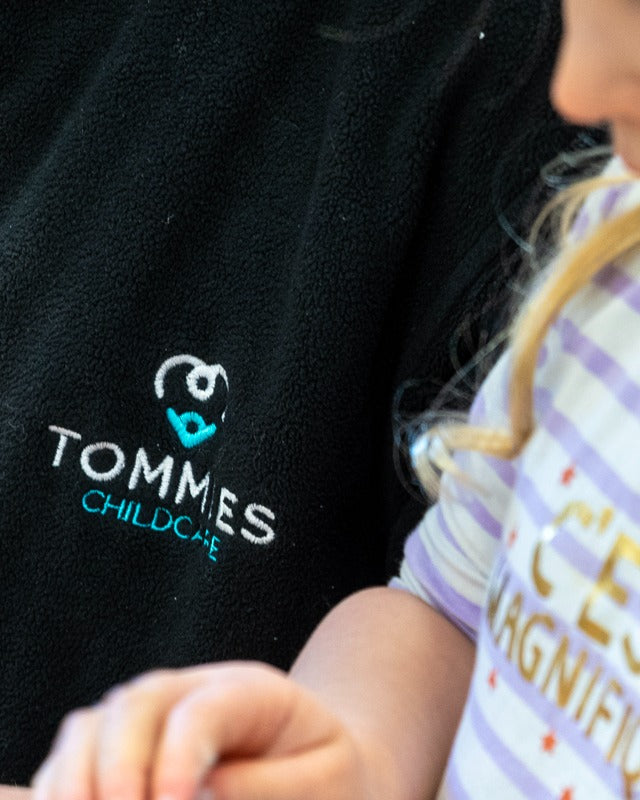Tommies Childcare logo embroidered on a navy staff fleece, worn in a nursery setting